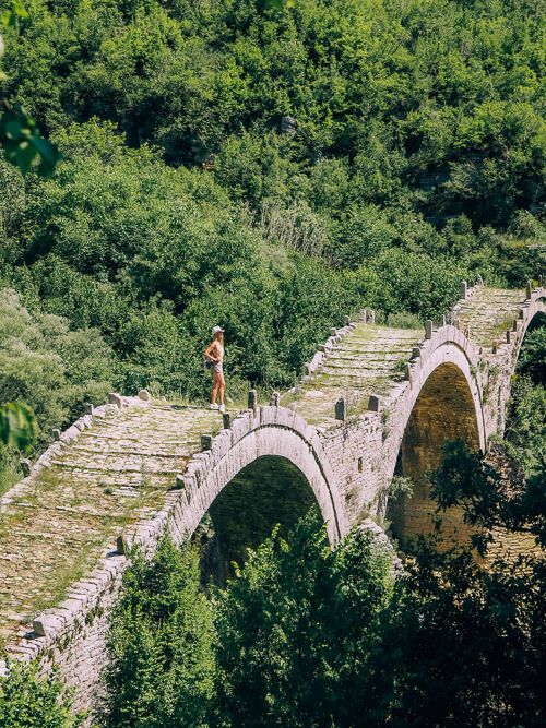 a woman standing on Plakidas bridge, a traditional three-arched stone bridge near Zagori villages