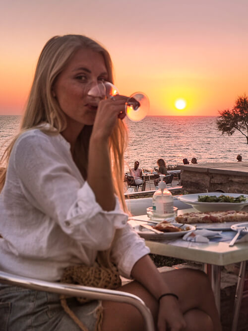 a woman sipping wine at a restaurant and enjoying a sunset