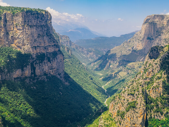 Vertical rock walls and green vegetation of Vikos Gorge viewed from Beloi viewpoint in Zagori, Greece.