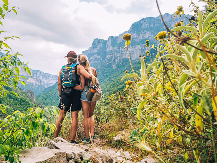 A couple hiking Vikos Gorge in Greece and admiring the view of the massive canyon.