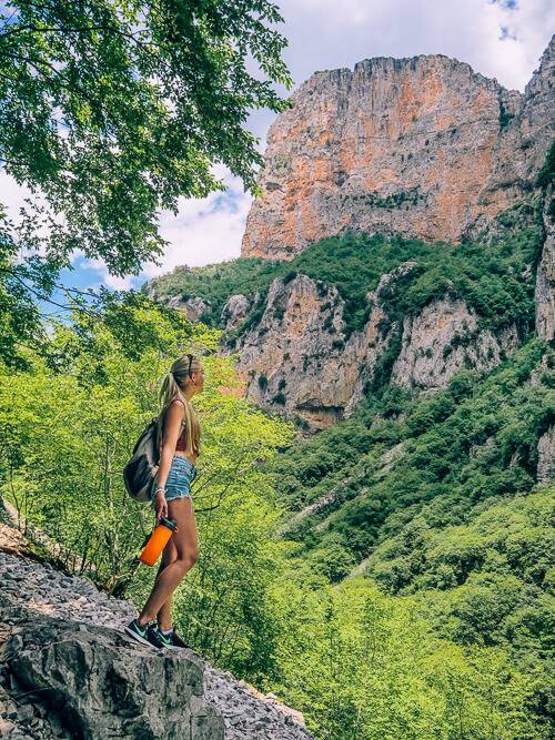 a woman hiking Vikos Gorge through rich and unique flora and dramatic landscape