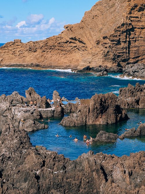 People swimming between brown lava rocks in the natural pools at Porto Moniz.