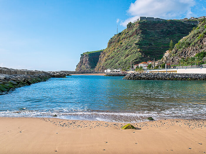 The popular Calheta Beach next to tall green cliffs, one of the few sandy beaches in Madeira.