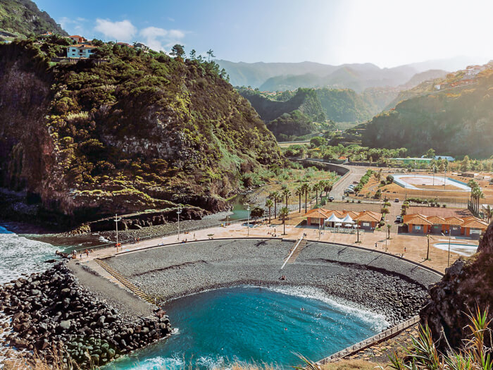 Lush green mountains and a small grey pebble beach at Faial Beach Club on Madeira island.