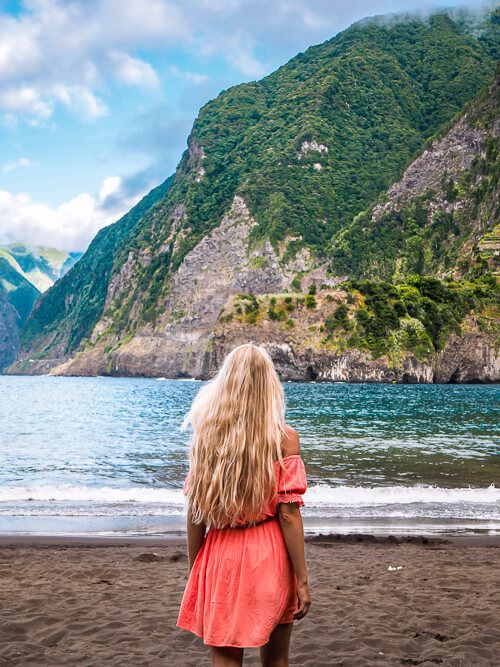 Me wearing a pink dress and walking along Seixal Beach with imposing green mountains in the background.