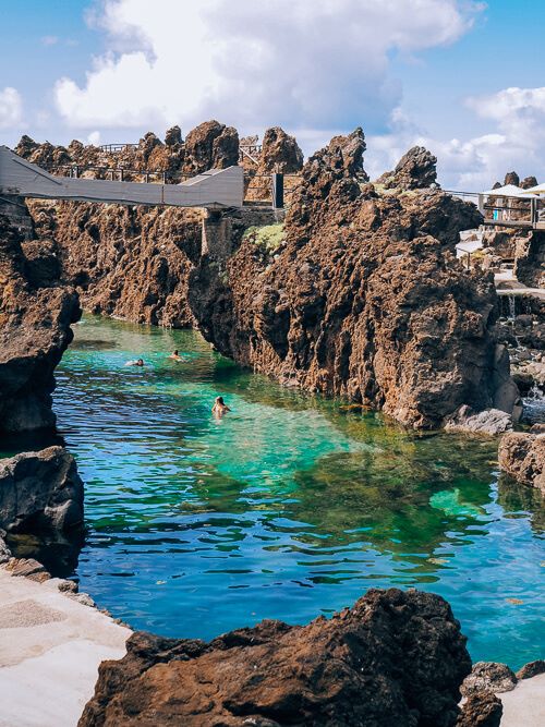 A pool of emerald water surrounded by jagged brown volcanic rocks at Cachalote Natural Pools in Porto Moniz.