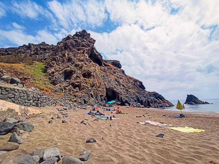 Rugged volcanic cliffs and brown sand at Prainha Beach, one of the best sandy beaches in Madeira.