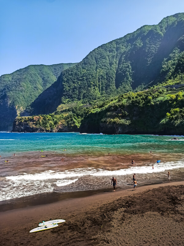 Seixal black sand beach in Madeira with turquoise waves rolling in, surfboards on the sand, and green cliffs surrounding the bay, one of the best sandy beaches in Madeira.