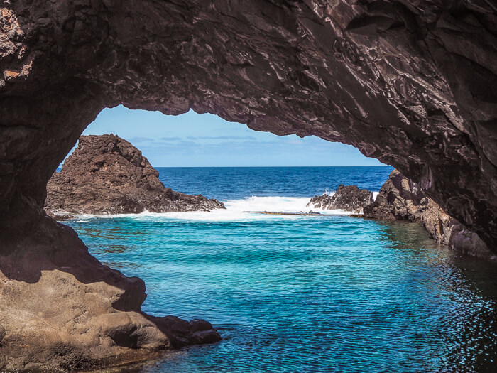 A large brown rock arch towering above one of the natural pools in Seixal.