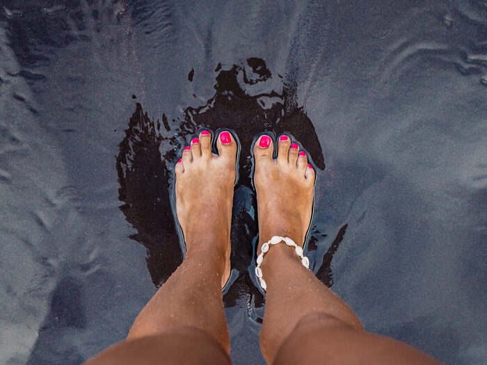 My two feet with pink toe nails on the black sand on Seixal Beach, Madeira Island