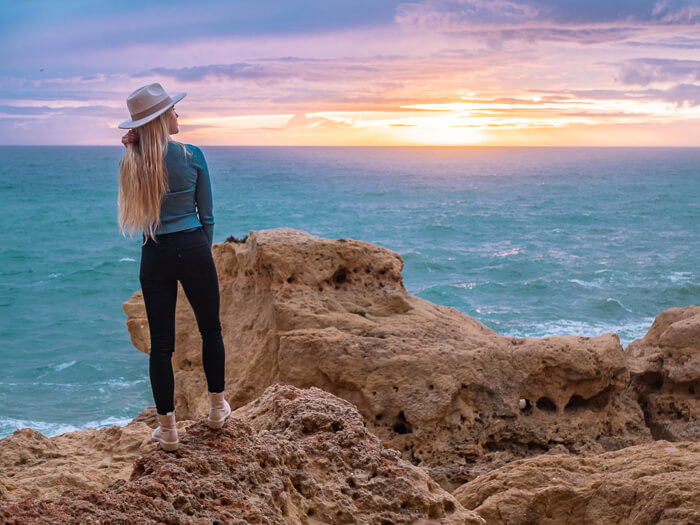 Me standing on a rock watching the colorful sunset, one of the best things to do in the Algarve in winter