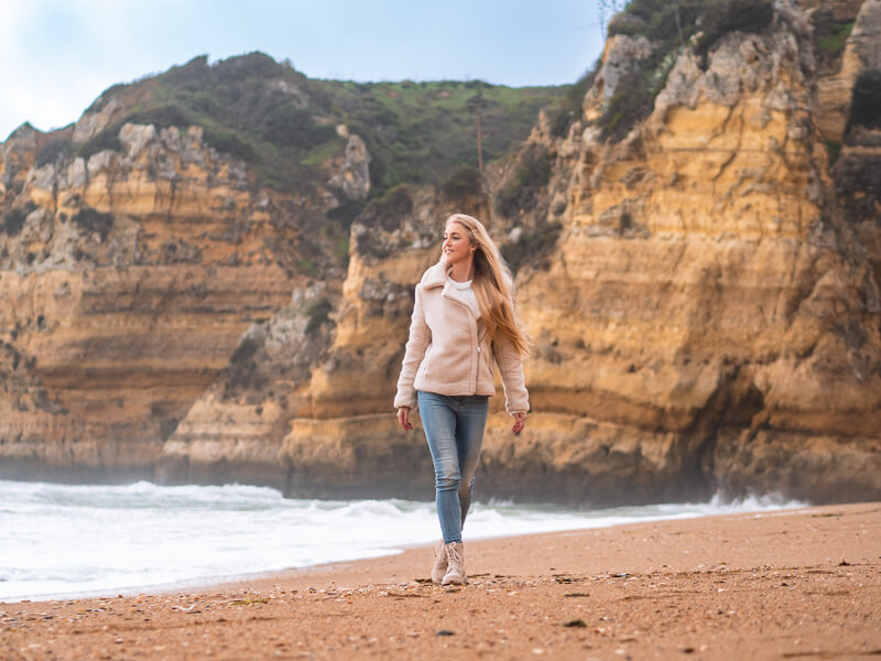 A woman walking along the sandy Praia da Dona Ana beach in winter in Algarve, Portugal