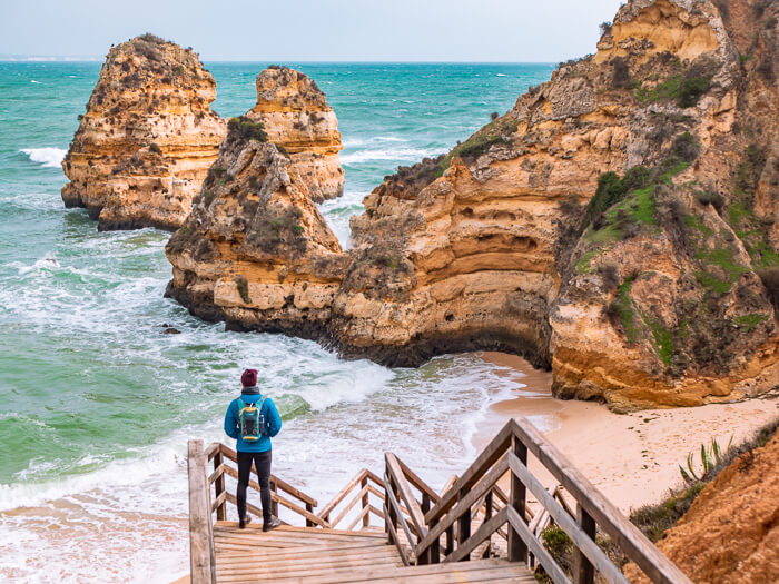 A man standing on a staircase and admiring the limestone cliffs at Praia do Camilo in Algarve in winter.
