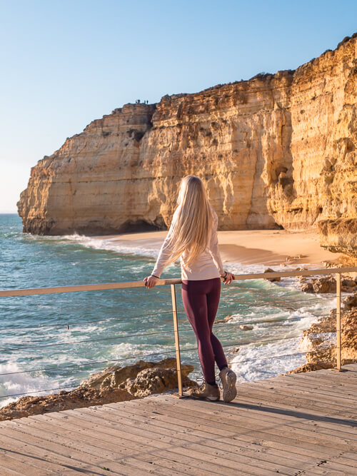 A woman enjoying a view of an empty golden sand beach, one of the reasons to visit Algarve in winter.