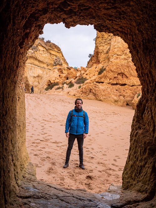 A man standing in front of a tunnel carved into limestone cliff at Praia dos Estudantes