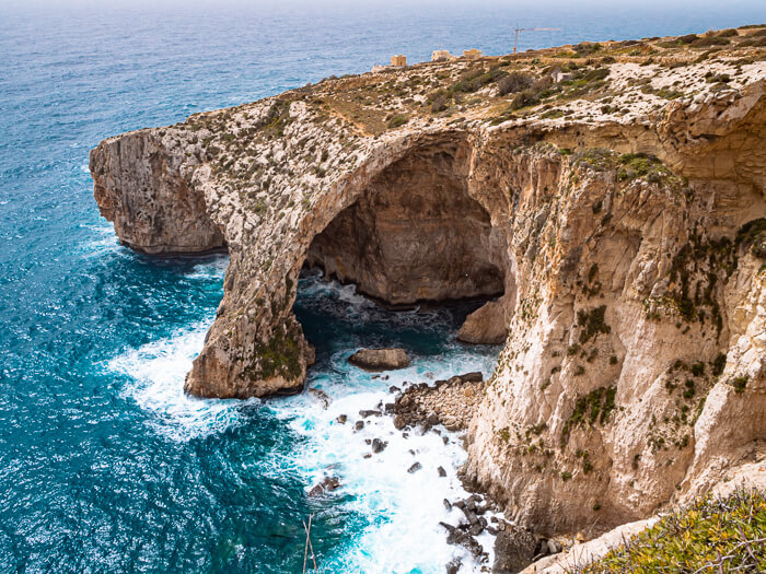 A large rock arch rising from turquoise sea at Blue Grotto, one of the highlights of this 7-day Malta itinerary