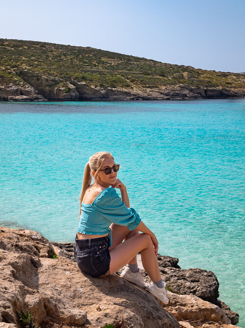 A woman sitting on a rock with a backdrop of vibrant turquoise water of the Blue Lagoon in Malta