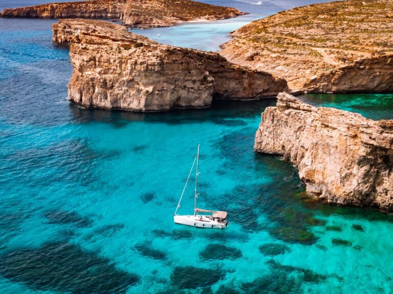 A white sailing boat surrounded by vibrant turquoise sea and beige cliffs in the background at Comino, Malta.