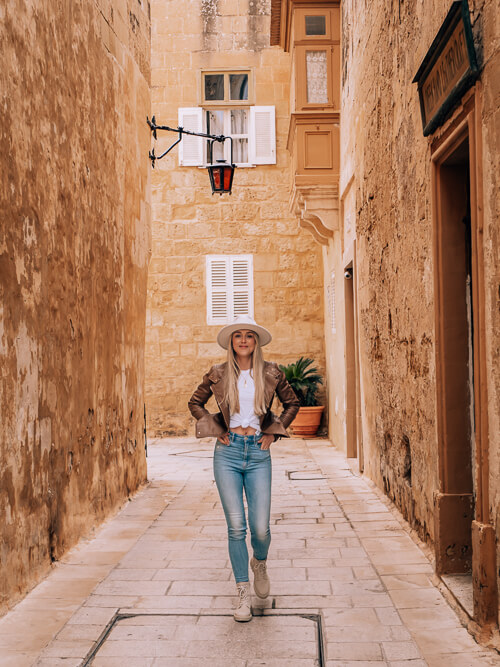 a woman walking along a narrow alleyway in the fortified town of Mdina in Malta