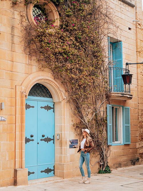 A quaint limestone building with a blue door and bougainvillea tree in Mdina, one of the best Malta Instagram spots