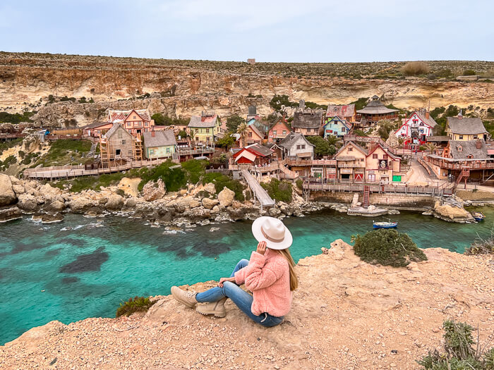 a woman sitting on a cliff and admiring the view over Popeye Village in Malta