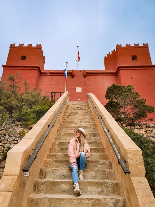 a woman sitting on stairs leading up to the Red Tower of Malta near Mellieha