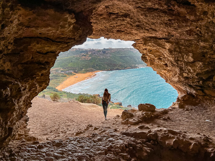 A woman standing at the mouth of Tal-Mixta cave overlooking the scenic Ramla Bay in Malta