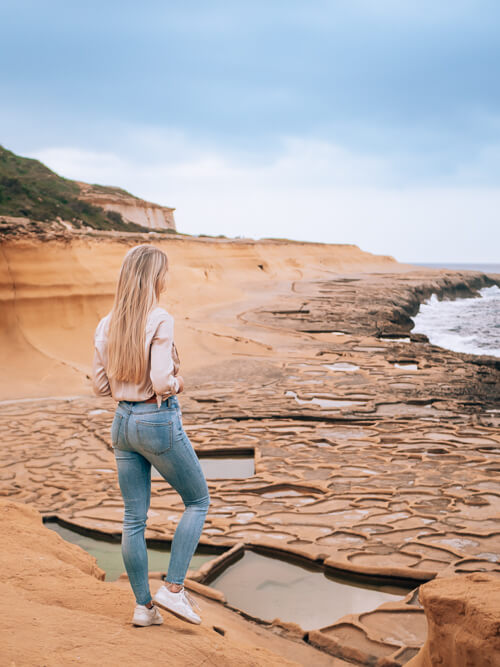 a woman standing on a cliff overlooking the ancient salt pans of Gozo island