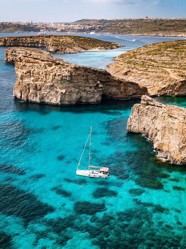 a white sailing boat surrounded by vibrant blue water and steep cliffs at Crystal Lagoon on Comino Island in Malta
