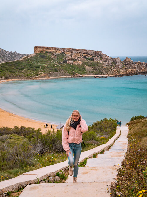 A woman standing on a staircase leading down to Ghajn Tuffieha Beach, one of the top Instagram spots in Malta