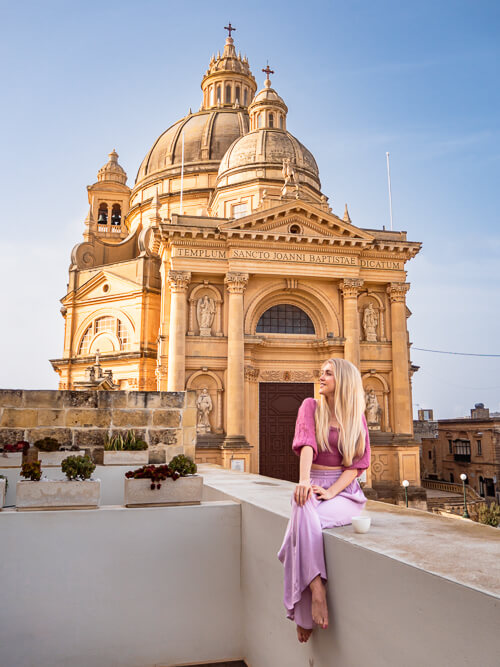 A woman sitting on a balcony in front of the huge Rotunda St. John Baptist Church, one of the top Gozo Instagram spots