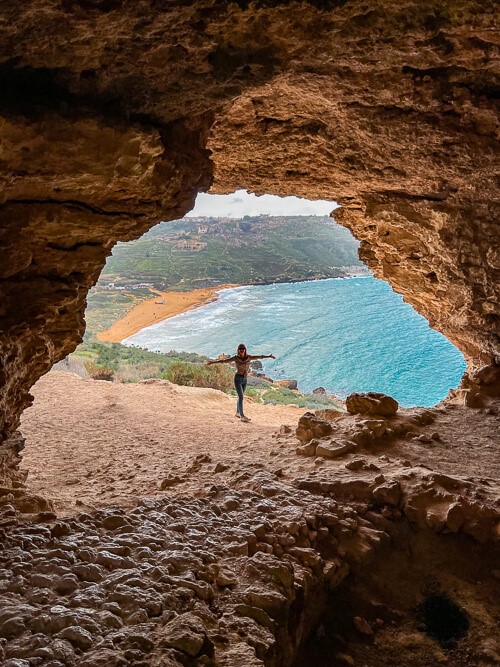 A woman standing at the mouth of the Tal Mixta Cave, one of the most amazing Malta Instagram spots
