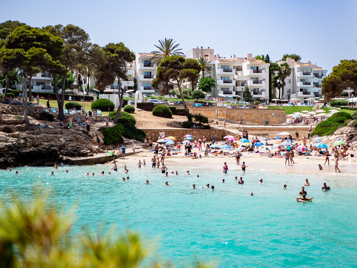 People bathing in the turquoise waters of Cala d'Or, a lovely beach town to include in your Mallorca road trip.