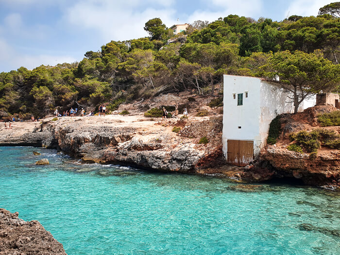 A small white boathouse overlooking a natural pool with turquoise water at Cala S'Almunia. 