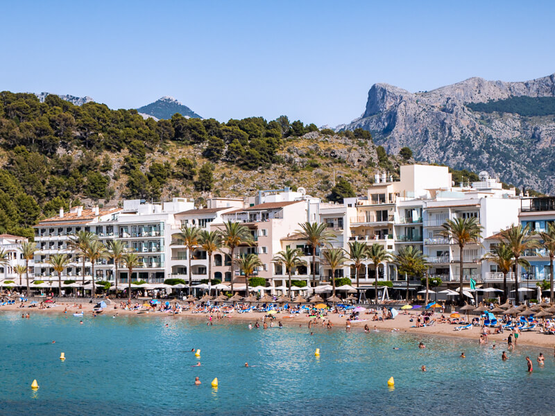 A sandy beach with azure water lined with palm trees in the seaside resort town Port de Soller.