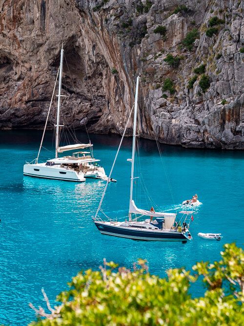 White sailboats floating in azure water in Sa Calobra bay.