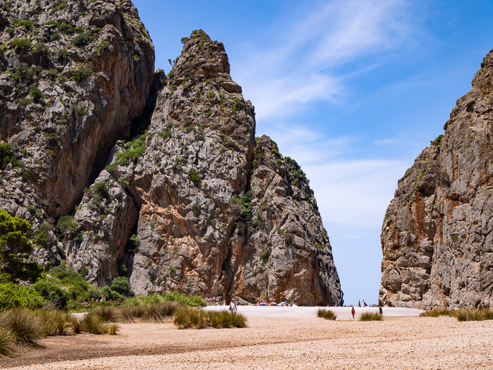 Torrent de Pareis canyon with towering rock walls and a sandy beach on a sunny day.