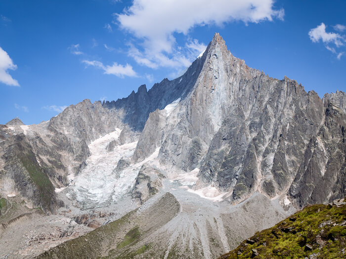 The colossal grey Aiguille du Dru mountain with its sharp peak and a backdrop of bright blue skies