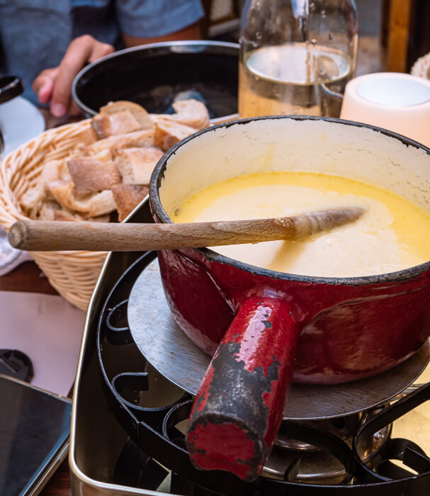 a red metal pot with cheese fondue and a basket of crusty bread pieces, a classic dish in the Alps region