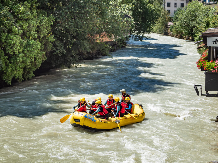 A group of people sitting in a yellow inflatable boat and doing whitewater rafting, one of the top summer activities in Chamonix