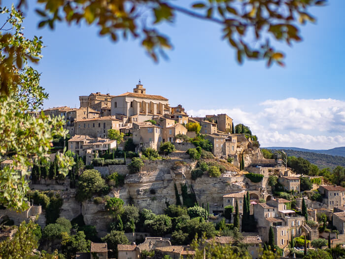 A panoramic view of the medieval hilltop village of Gordes with its beige stone houses on a sunny day with blue sky.