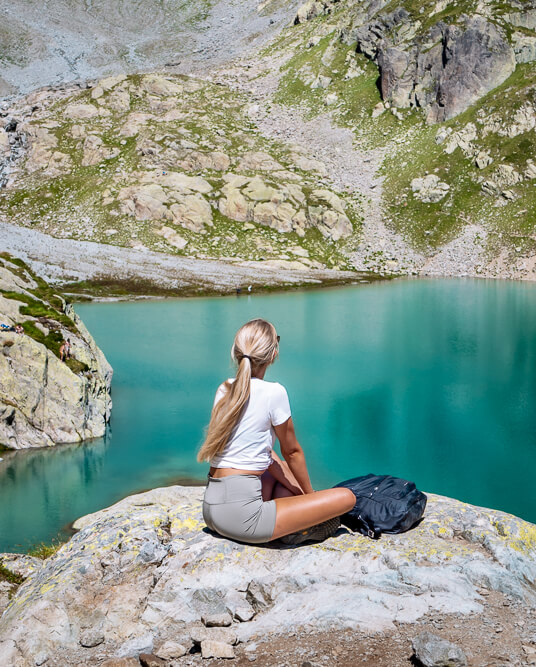 A woman sitting on a rock overlooking the blue-green Lac Blanc lake in the French Alps