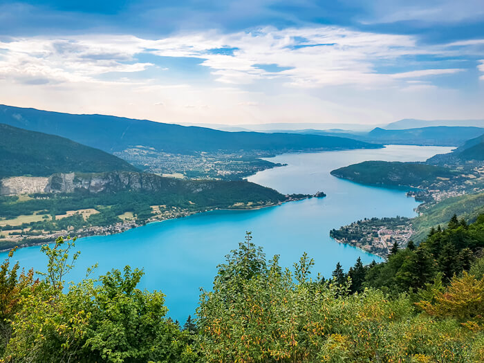 Panoramic view of the turquoise-blue Lake Annecy nestled between green hills; one of the most beautiful lakes in France