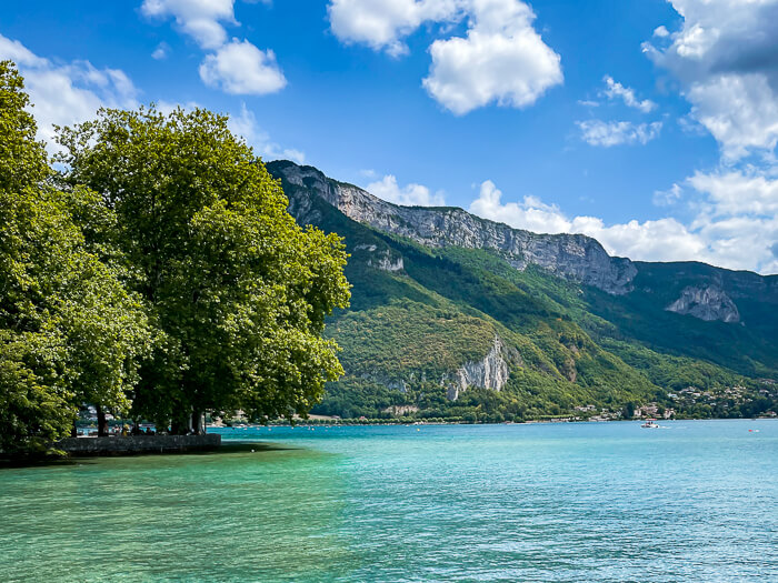 Dramatic forest-covered mountains and crystal blue water at Lac d'Annecy, the cleanest lake in Europe