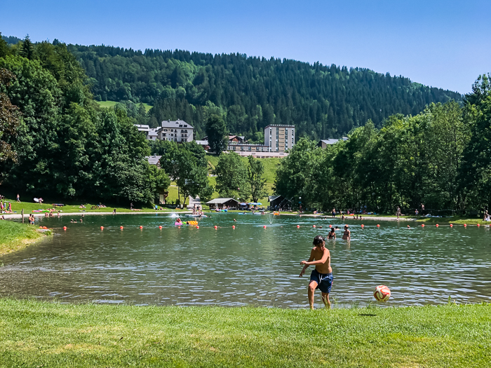 A boy playing ball on the grassy shores of the small family-friendly Lake Flumet in the Haute Savoie region in France