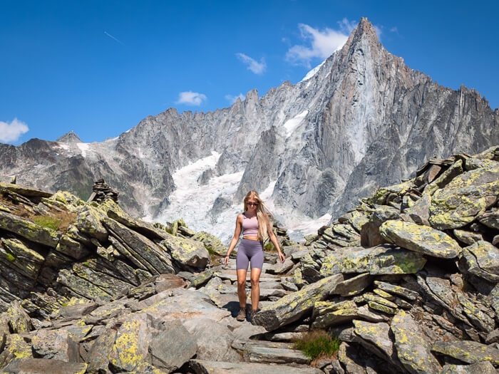 A woman walking down rocky steps on the Grand Balcon Nord hike with the giant grey Aiguille du Dru mountain looming in the background
