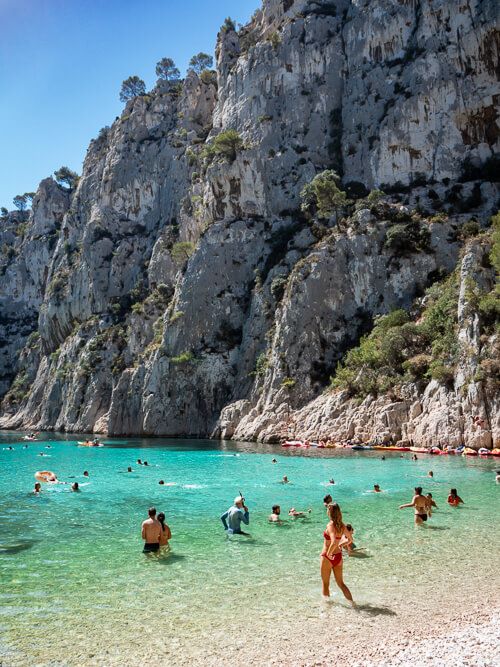 People swimming at a beach with bright blue water and tall cliffs at Calanques National Park in Provence