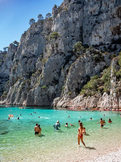 People swimming at a beach with bright blue water and tall cliffs at Calanques National Park in Provence.