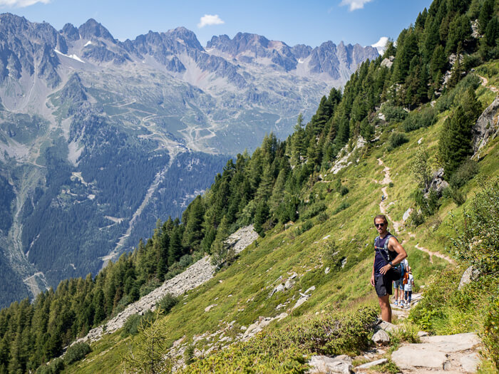 A man standing on the Grand Balcon Nord hiking trail amidst an alpine grassland with a backdrop of Aiguilles Rouges mountain range