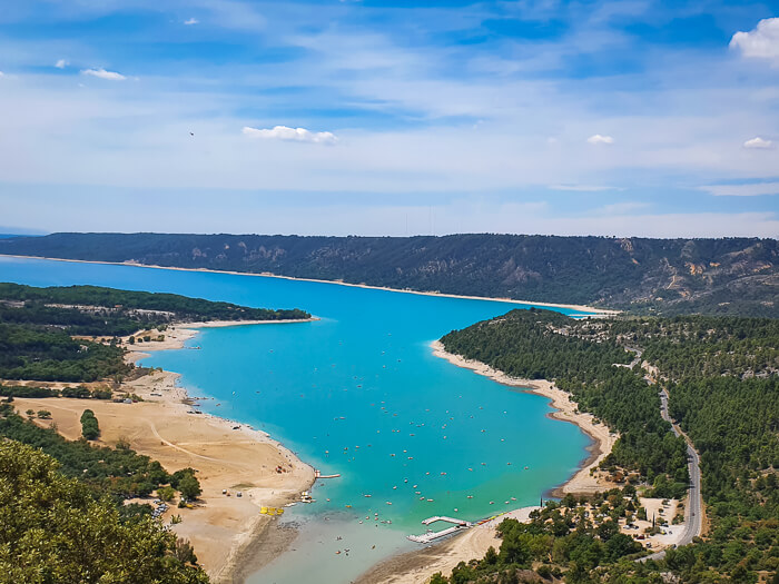 a panorama of the turquoise Lake of Sainte-Croix and the surrounding forest-covered hills, viewed from Verdon Gorge